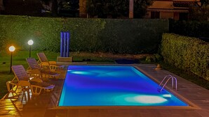 Een rechthoekig zwembad met een blauwe tint, omgeven door een houten terras en ligstoelen.