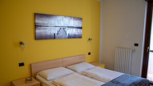 A bedroom with a wooden bed, two bedside tables, a nightstand, a painting of a pier, and a radiator.