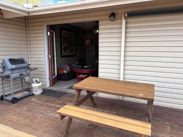 Une table de pique-nique et un barbecue en bois sont installés sur une véranda, dont une porte donne accès à l’intérieur.