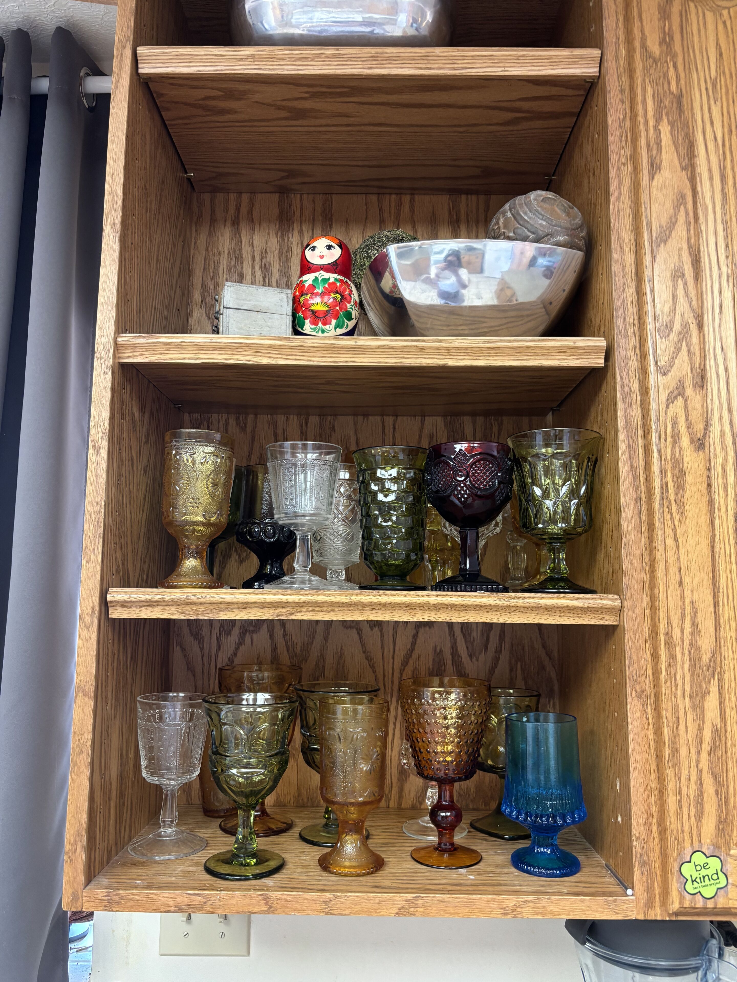 A wooden cabinet with glassware and a matryoshka doll.