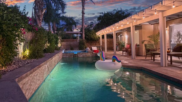 A pool area with a clear view of the water, a lounge chair, and a covered seating area with string lights. - Posh Villa Sleeps 12 w/ 4 bedroom, 3 bath Pool & Spa (Indio)