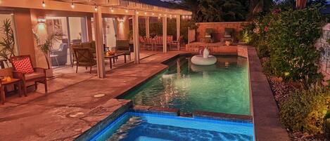 Una piscina con jacuzzi, mobiliario exterior e iluminación con luces colgantes.