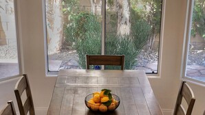 A dining table with a fruit bowl, surrounded by chairs, in a room with large windows and a chandelier. - Posh Villa Sleeps 12 w/ 4 bedroom, 3 bath Pool & Spa (Indio)