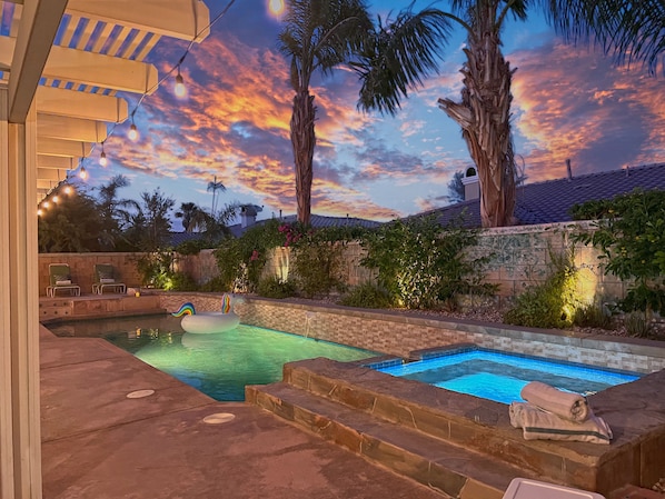 A backyard with a swimming pool, palm trees, and string lights.