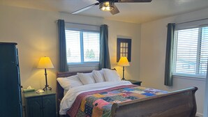 A neatly made bed with a colorful quilt, two bedside lamps, a ceiling fan, and a window with curtains. - #6 Home in the Heart of Utah (Torrey)