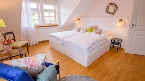 A bedroom with a large bed, two bedside tables, a chair, a small table with a lamp, and a window with curtains. - Werts HOF Ferienwohnung 2 (Rauschenberg)