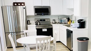 A modern kitchen with white cabinets, stainless steel appliances, a microwave, a toaster, and a coffee maker.