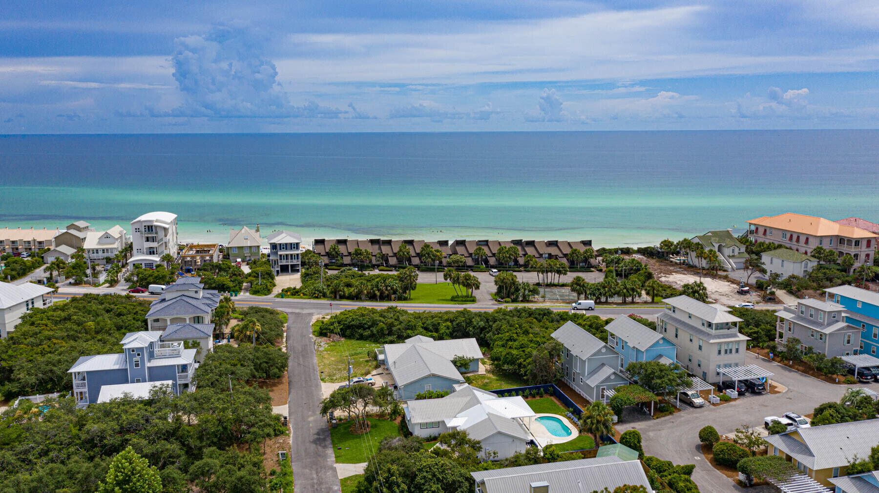 A coastal residential area with houses, a swimming pool, and a beach in the background.