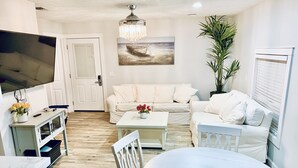 A living room with a white sofa, a round dining table, a TV, and a chandelier.