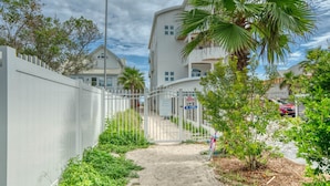 A gated pathway leading to a building with a private beach access sign, surrounded by greenery and a parked car.