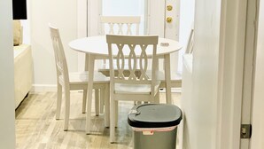 A small, clean room with a white door, a round table, two chairs, and a trash bin.