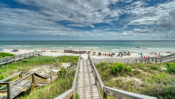 A wooden boardwalk leading to a beach with umbrellas and beach chairs.