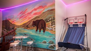 A room with a mural of a bear in a river, a basketball hoop, and a bar area with stools. - Checkout our weekday discount! w/Central AC. (Big Bear)