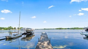 A wooden dock extending into calm water with boats docked on either side. - Lakefront Cottage on Webster Lake with Beautiful Sunsets, 2 bed, 1 bath (North Webster)