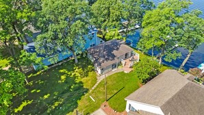 An aerial view of a residential area with a house featuring a large deck and a view of a lake. - Lakefront Cottage on Webster Lake with Beautiful Sunsets, 2 bed, 1 bath (North Webster)