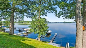 A lakeside view with a dock, boats, and a grassy area. - Lakefront Cottage on Webster Lake with Beautiful Sunsets, 2 bed, 1 bath (North Webster)
