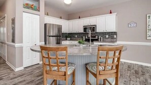 A modern kitchen with white cabinetry, stainless steel appliances, and a central island with two wooden chairs. - Blue Water; Oceanview condo, Atlantic Beach (Atlantic Beach)