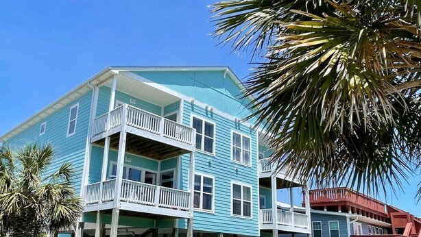 A multi-story building with balconies, a wooden fence, and a palm tree. - Blue Water; Oceanview condo, Atlantic Beach (Atlantic Beach)