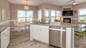 A modern kitchen with a central island, white cabinetry, and a dining area with wooden chairs. - Blue Water; Oceanview condo, Atlantic Beach (Atlantic Beach)
