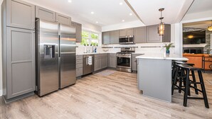 A modern kitchen with stainless steel appliances, grey cabinetry, and a central island with bar stools.