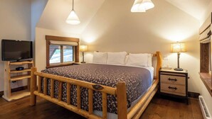 Une chambre à coucher avec un lit en bois, deux lampes de chevet, un téléviseur posé sur un meuble en bois et une fenêtre donnant sur un paysage.