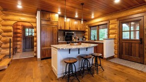Une cuisine de style rustique, avec des meubles en bois, un plan de travail en granit et un îlot central doté de tabourets.