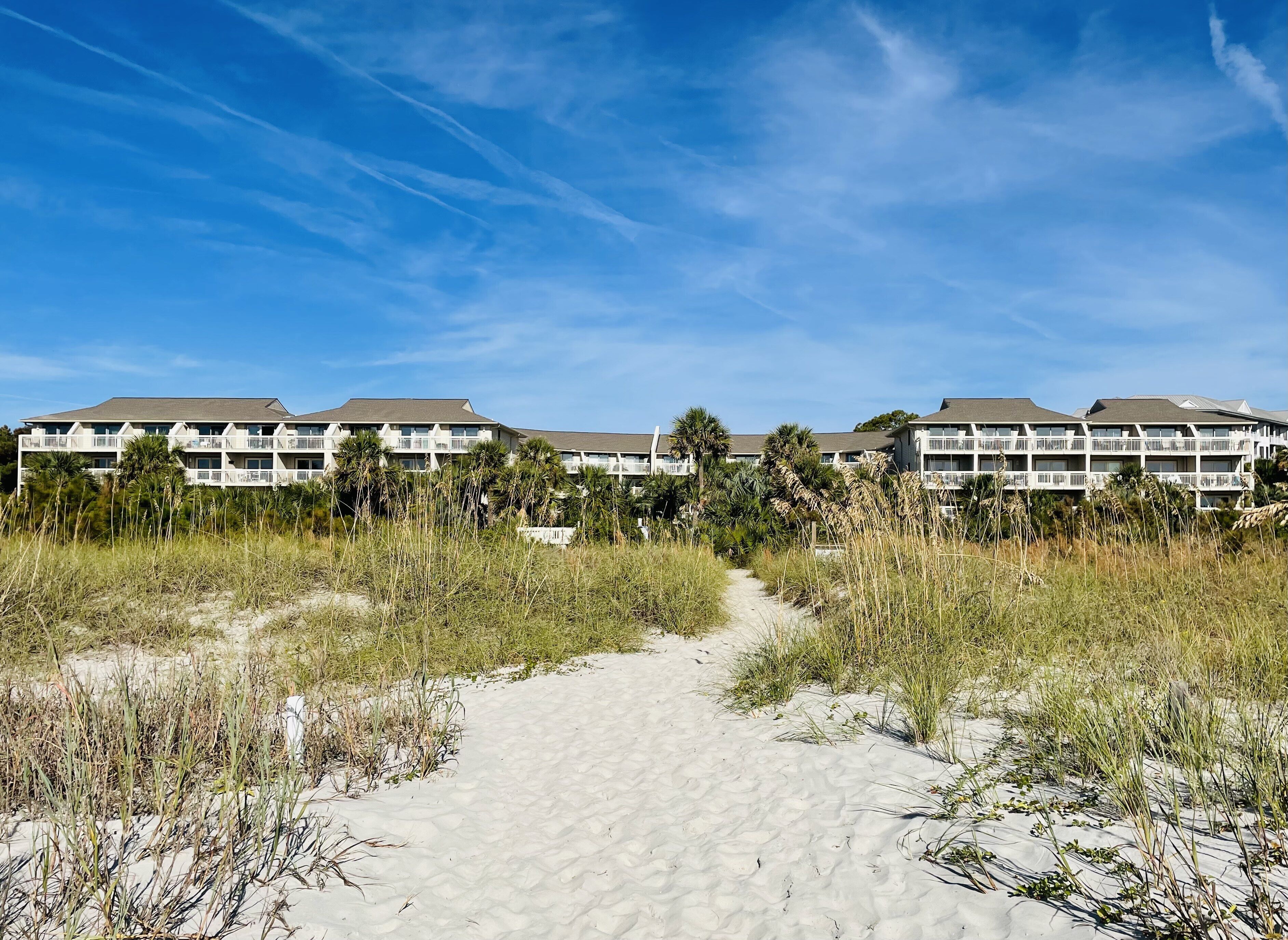 Een hotel aan het strand met meerdere gebouwen, een zandpad naar het strand en palmbomen.