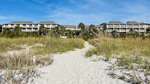 Ein Strandhotel mit mehreren Gebäuden, einem Sandweg, der zum Strand führt, und Palmen.