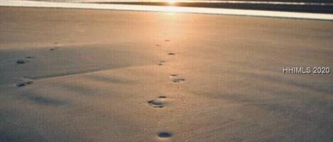 A beach with footprints leading towards the ocean at sunset.