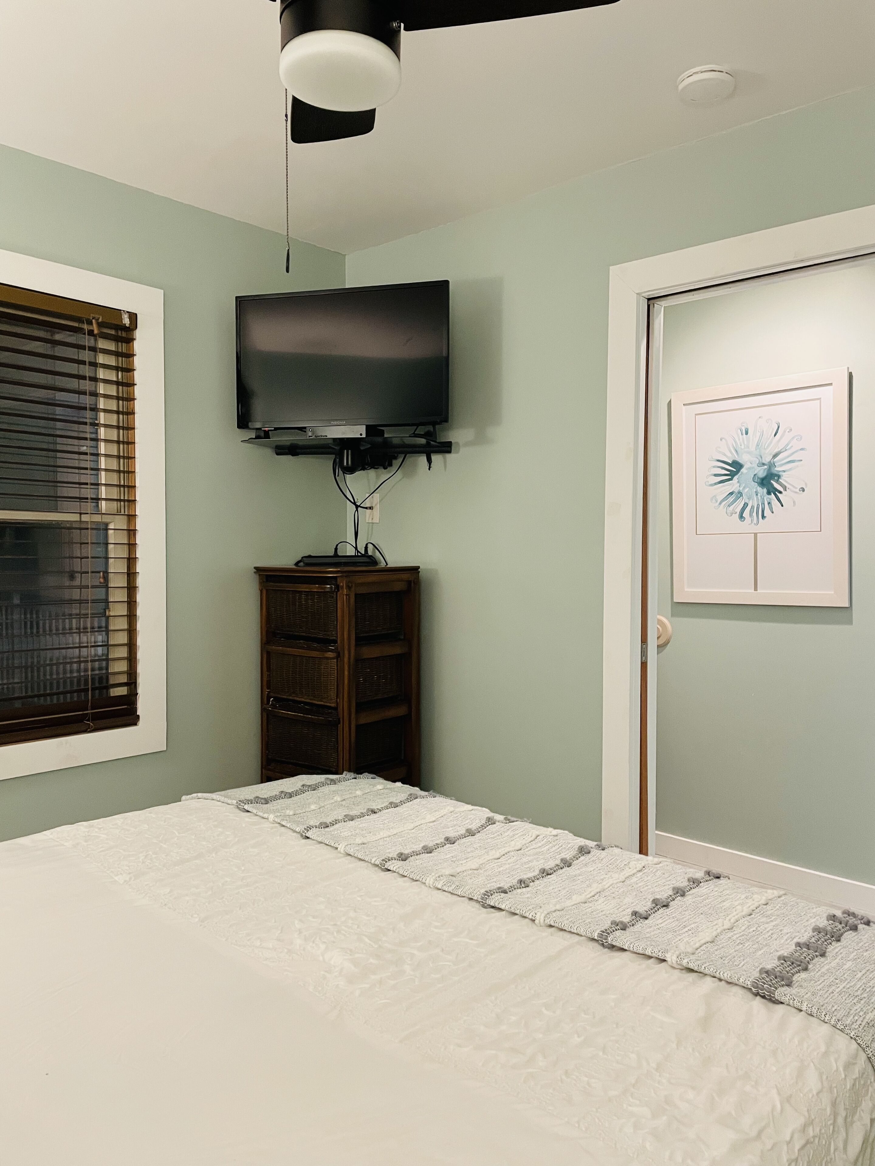 A bedroom with a bed, a television mounted on the wall, a wooden cabinet, and a door with a framed picture.