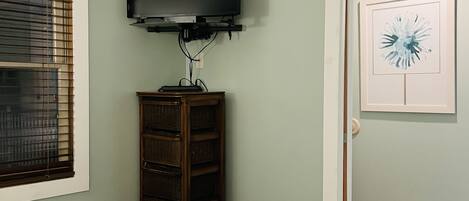 A bedroom with a bed, a television mounted on the wall, a wooden cabinet, and a door with a framed picture.
