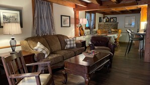 Ein gemütliches Wohnzimmer mit Holzbalkendecke, einem braunen Sofa, einem Holztisch und einem Essbereich mit Tisch und Stühlen.
