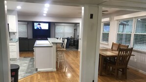 A modern kitchen with a central island, dining area with wooden chairs, and a TV in the background. - Lakehouse with Dock (Benton)