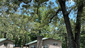 A cabin with a green roof, surrounded by trees and a grassy yard. - Lakehouse with Dock (Benton)