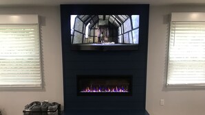 A fireplace with a TV screen above it, flanked by windows with blinds. - Lakehouse with Dock (Benton)