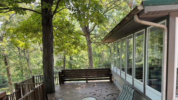 A covered porch with a wooden bench, two striped chairs, and a small table. - Lakehouse with Dock (Benton)