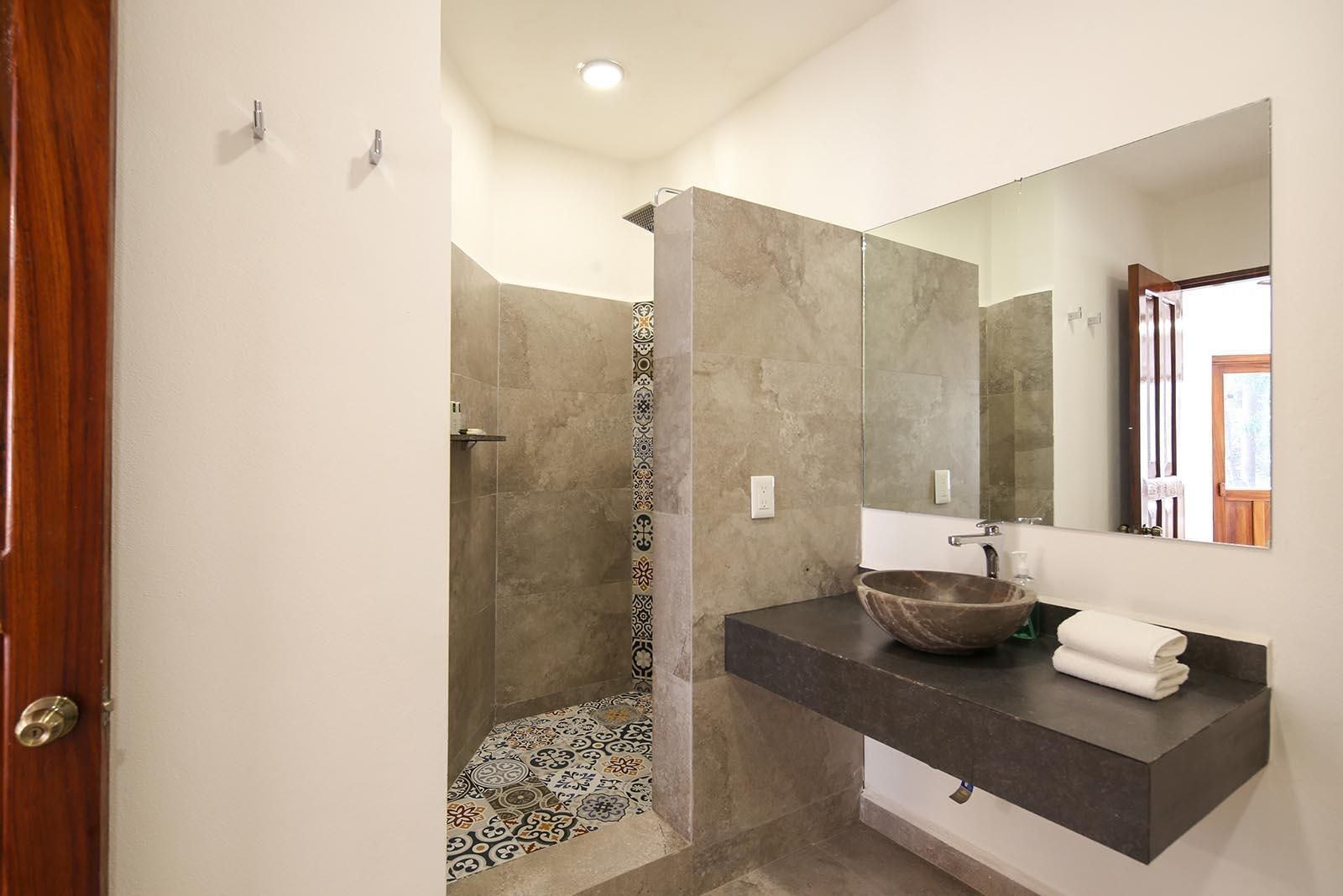 A modern bathroom with a walk-in shower, a large mirror, and a dark countertop.