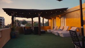 Eine Dachterrasse mit einer Pergola, Liegestühlen und Blick auf die Skyline.