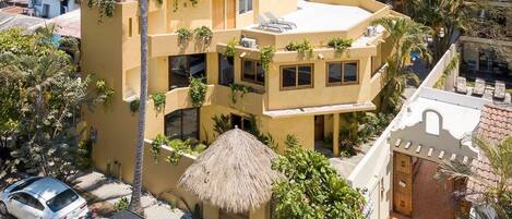 A multi-story building with a flat roof, surrounded by palm trees and other vegetation.