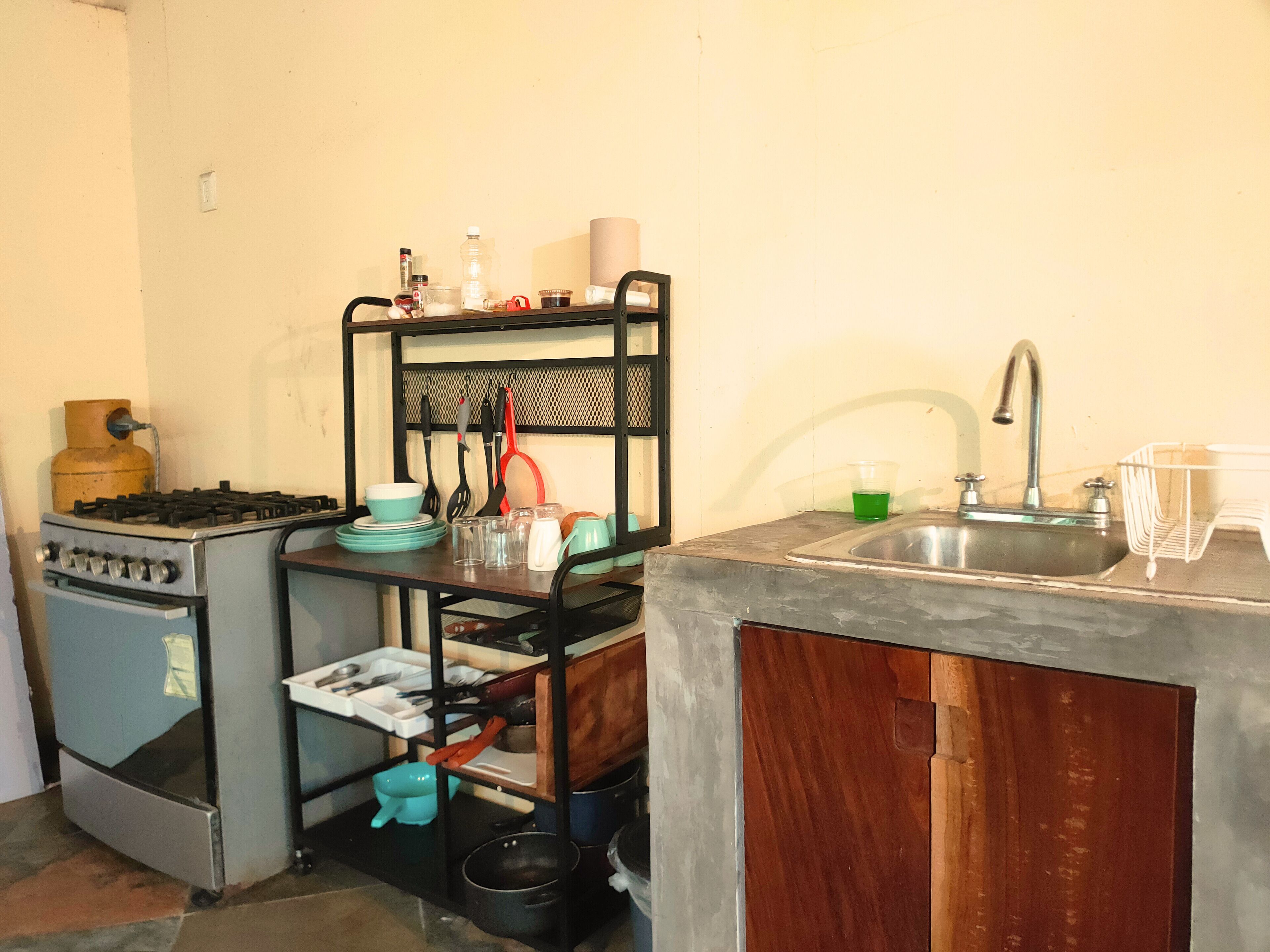 Cocina compacta con estufa a gas, pileta y un escurridor metálico con utensilios de cocina.
