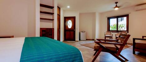 A hotel room with a bed, a dining area with chairs, a ceiling fan, and a window with a view.