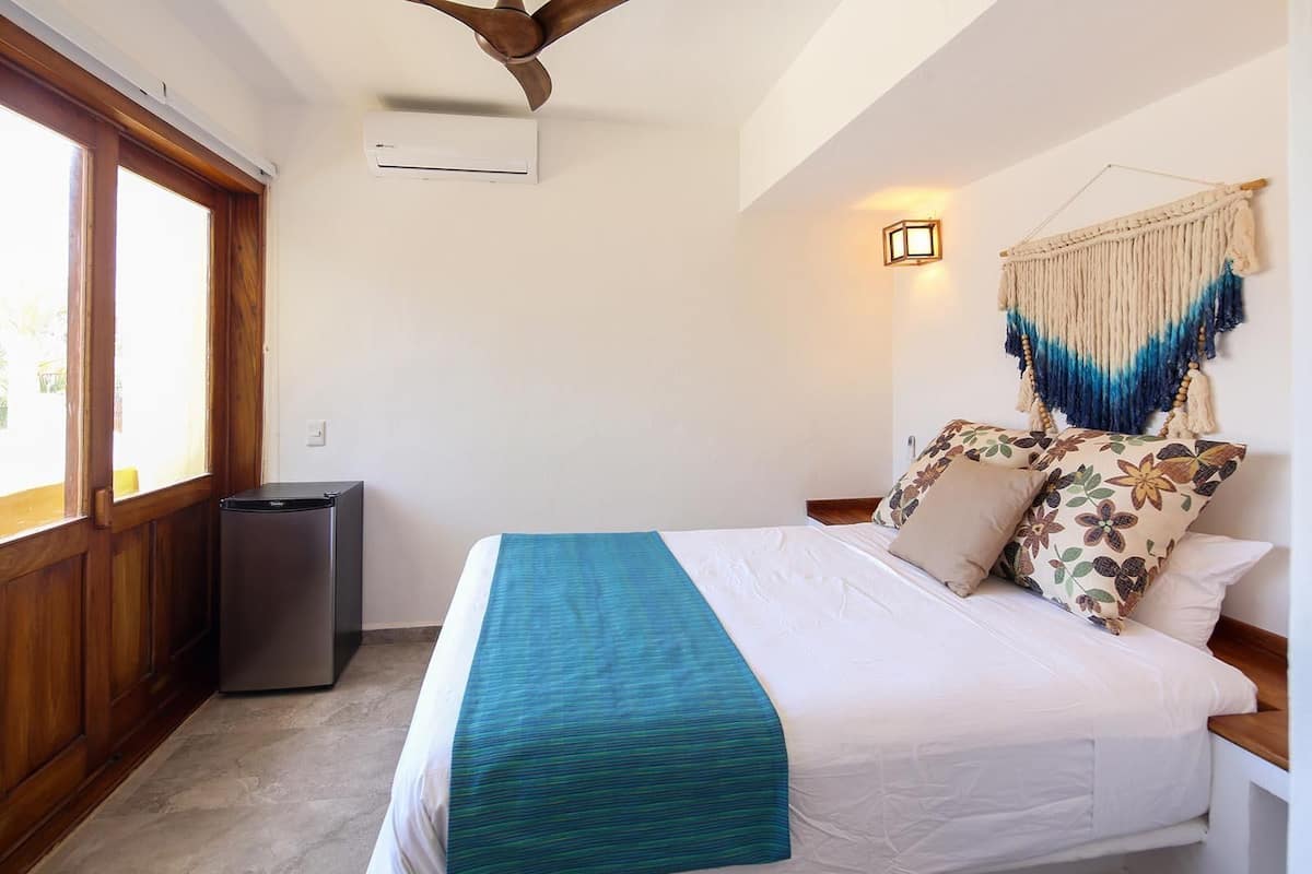 A bedroom with a bed, a small air conditioning unit, a wooden cabinet, and a wall-mounted light fixture.