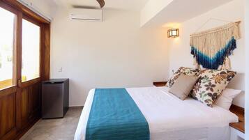 A bedroom with a bed, a small air conditioning unit, a wooden cabinet, and a wall-mounted light fixture.