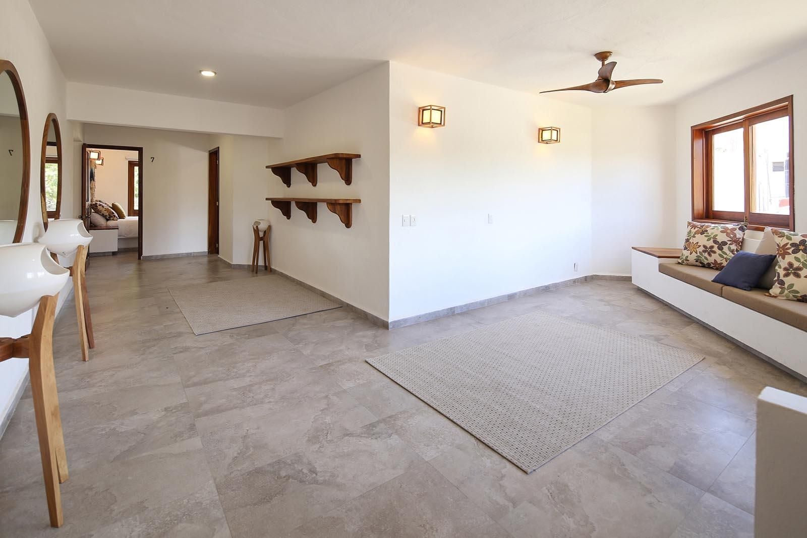 A spacious living area with a high ceiling, a ceiling fan, and a large window providing natural light.