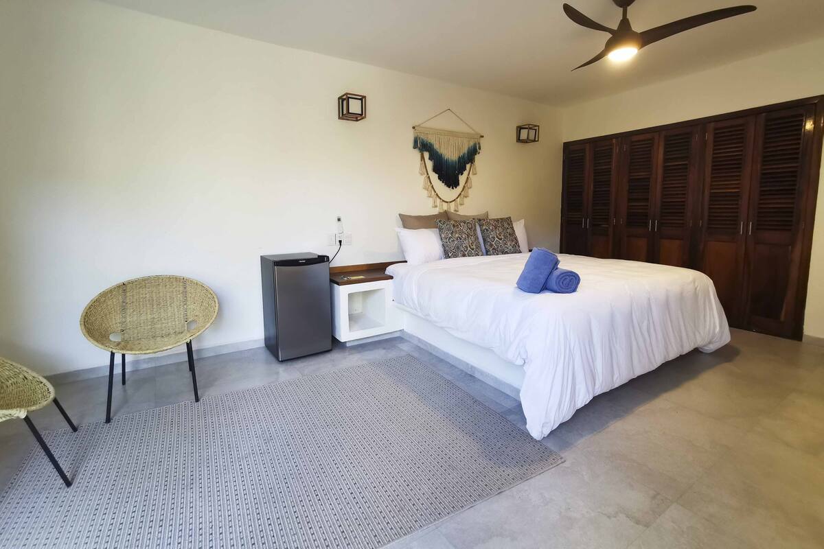 A bedroom with a bed, a small desk, a chair, a ceiling fan, and a wardrobe.