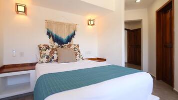 A bedroom with a large bed, two bedside tables, a wall-mounted light, and a hanging macrame piece.