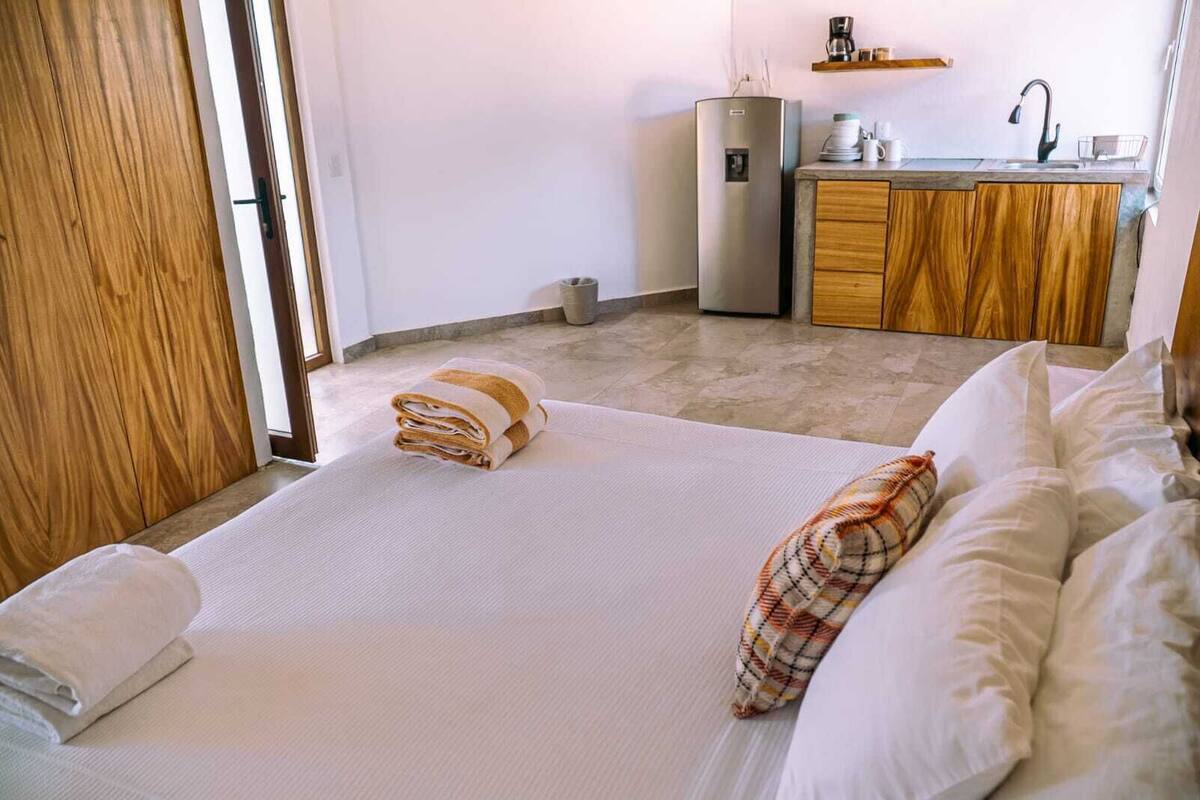 A hotel room with a bed, a wooden wardrobe, a kitchenette with a refrigerator, and a sink.