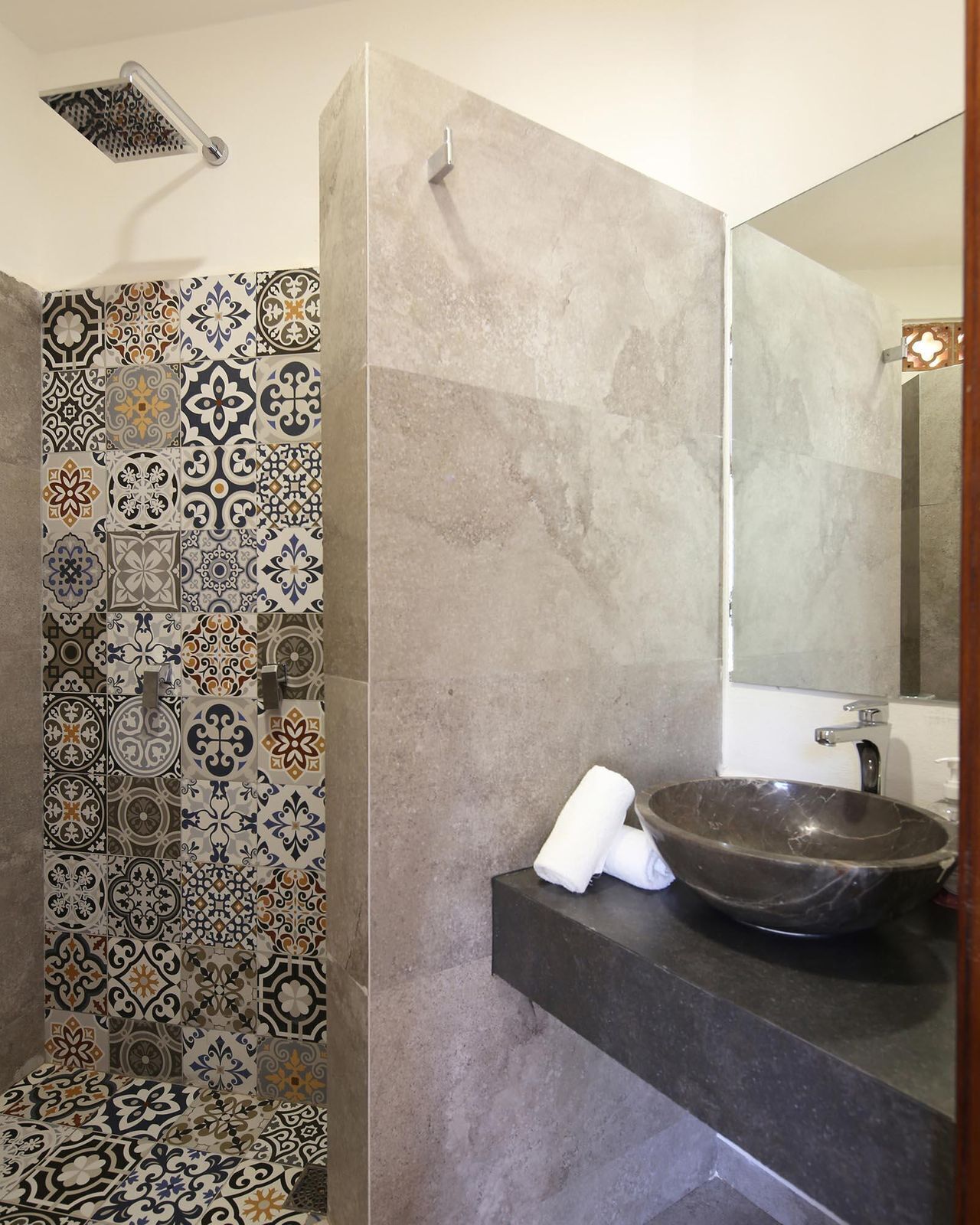 Ein Badezimmer mit einer Duschwand aus Mosaik, einem großen Spiegel und einem dunklen Marmorwaschbecken.