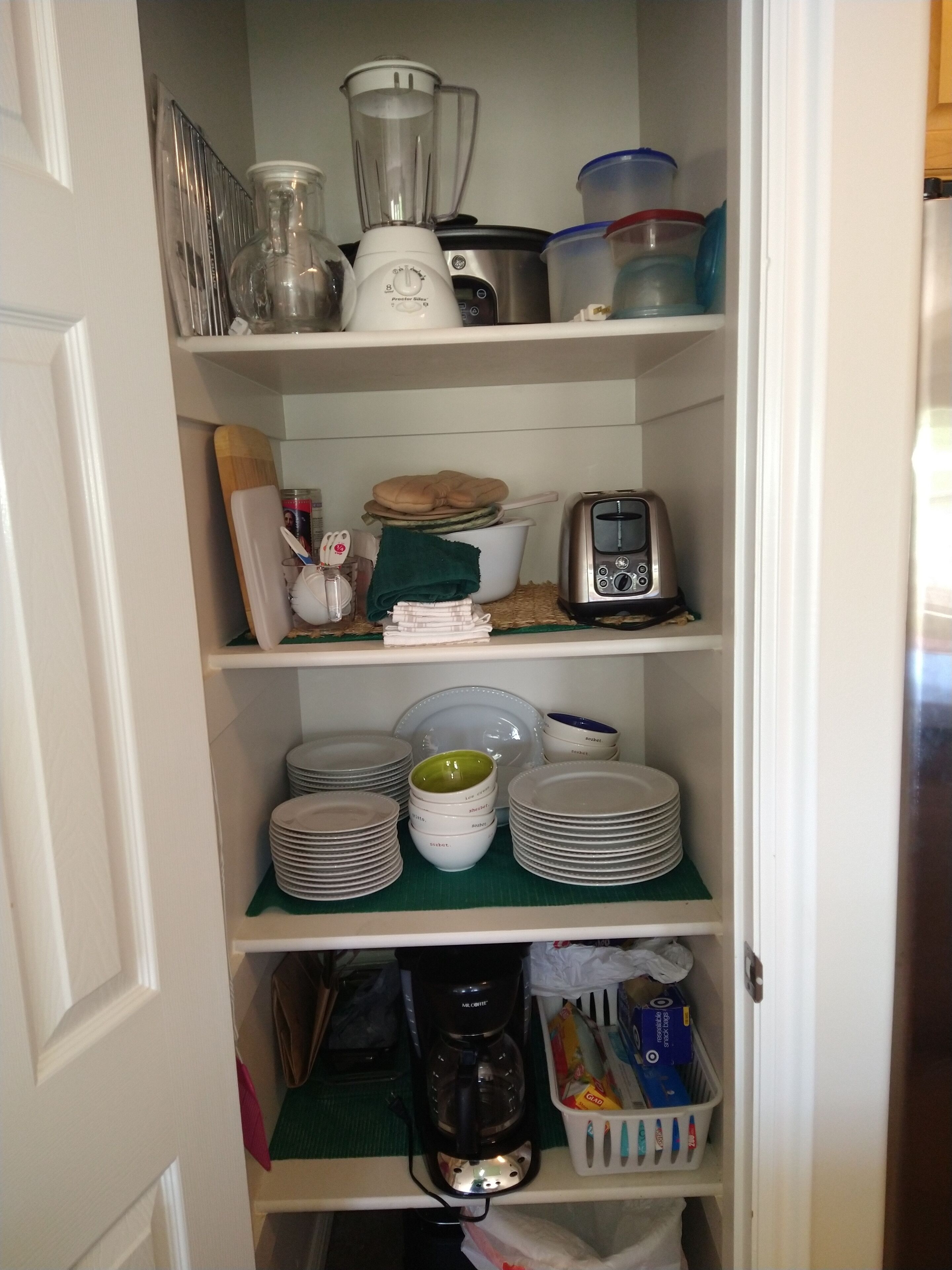 A kitchen pantry with shelves containing a blender, toaster, coffee maker, and various kitchen utensils.