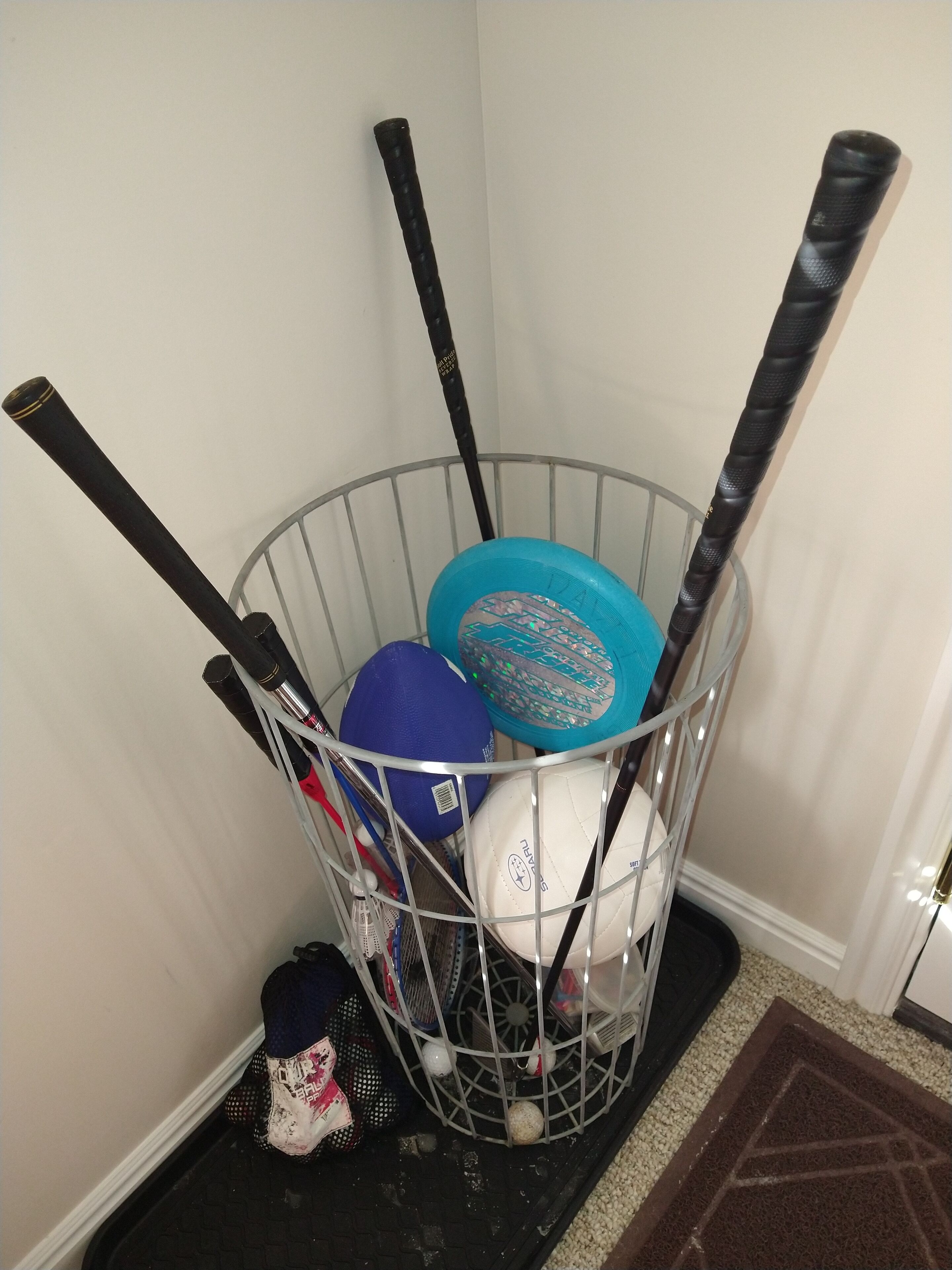 A metal basket containing sports equipment, including a blue and white ball, a tennis racket, and a black stick.